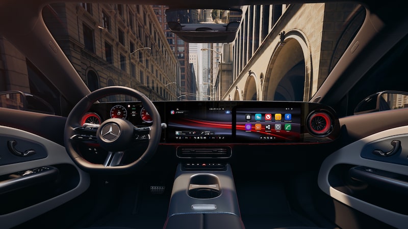 Das Interieur zeigt ein Lenkrad mit Mercedes-Benz Stern, drei nahtlos wirkende Displays im Armaturenbrett und rot beleuchtete Lüftungsdüsen.