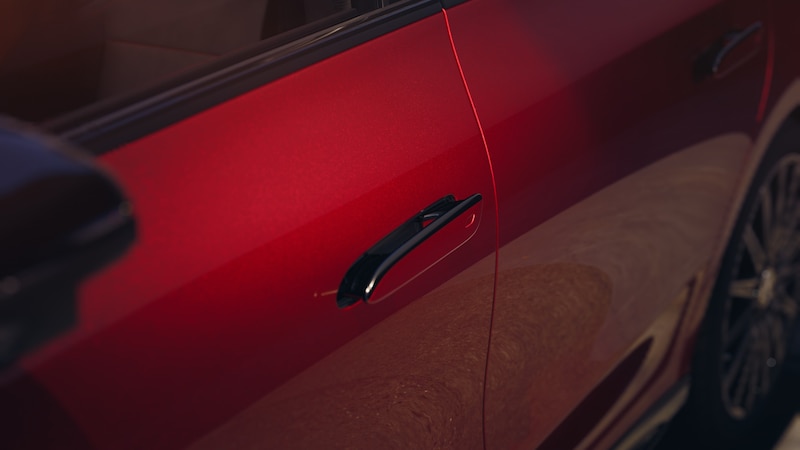 Die rote Fahrzeugseite des CLA Elektrisch zeigt einen flächenbündigen schwarzen Türgriff und ein aerodynamisch wirkendes Karosseriedesign.