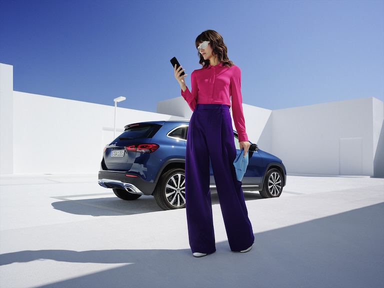 Women stands in front of the Mercedes-Benz GLA and is looking on her phone.