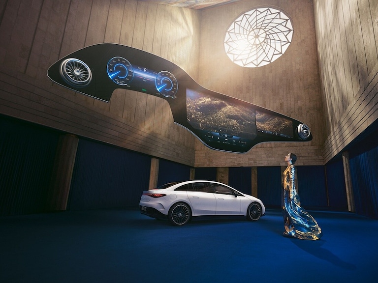 Woman standing in front of Mercedes-Benz EQ vehicle with the Hyperscreen hovering above her.