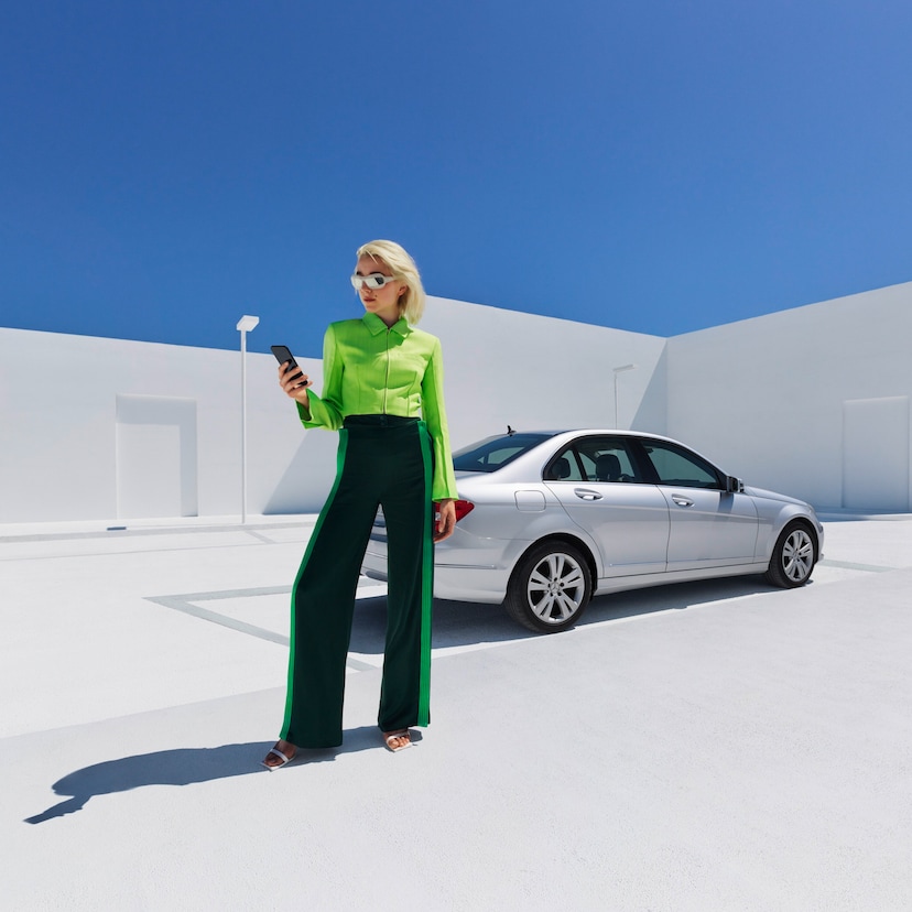 Programme d'avantages de service | Mercedes-Benz Une femme se tient devant sa Mercedes-Benz et consulte son smartphone.