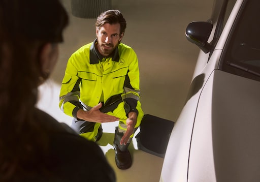 Assurance mobilité | Mercedes-Benz Un technicien agenouillé à côté d'un véhicule Mercedes-Benz et s'adressant à un client.