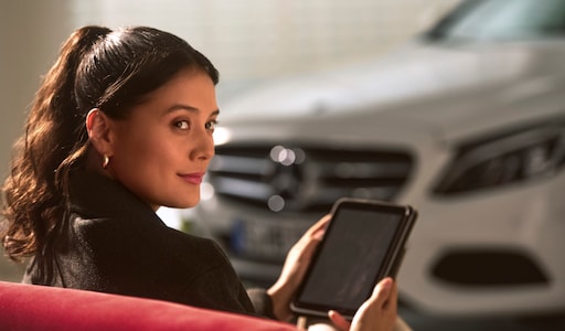 Préservation de la valeur | Mercedes-Benz Une personne assise à côté d'un véhicule Mercedes-Benz, une tablette à la main.