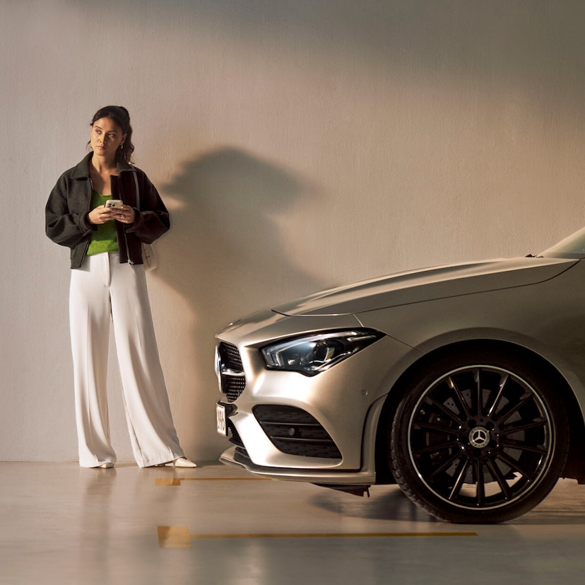 Service Select | Mercedes-Benz Une femme se tient devant un véhicule Mercedes-Benz.