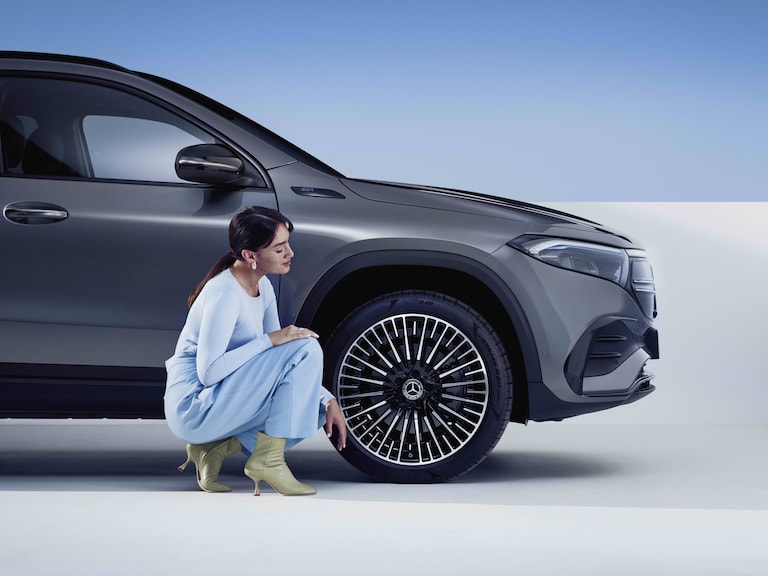 A woman looks at the front wheel of her Mercedes-Benz.