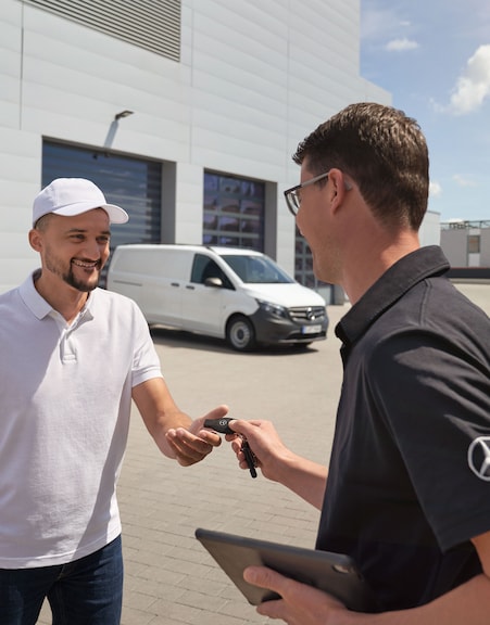 Mercedes-Benz | Wartung | Abholung und Anlieferung Mercedes-Benz Servicemitarbeiter bei der Schlüsselübergabe an einen Kunden mit einem weißen Mercedes-Benz Vito im Hintergrund.