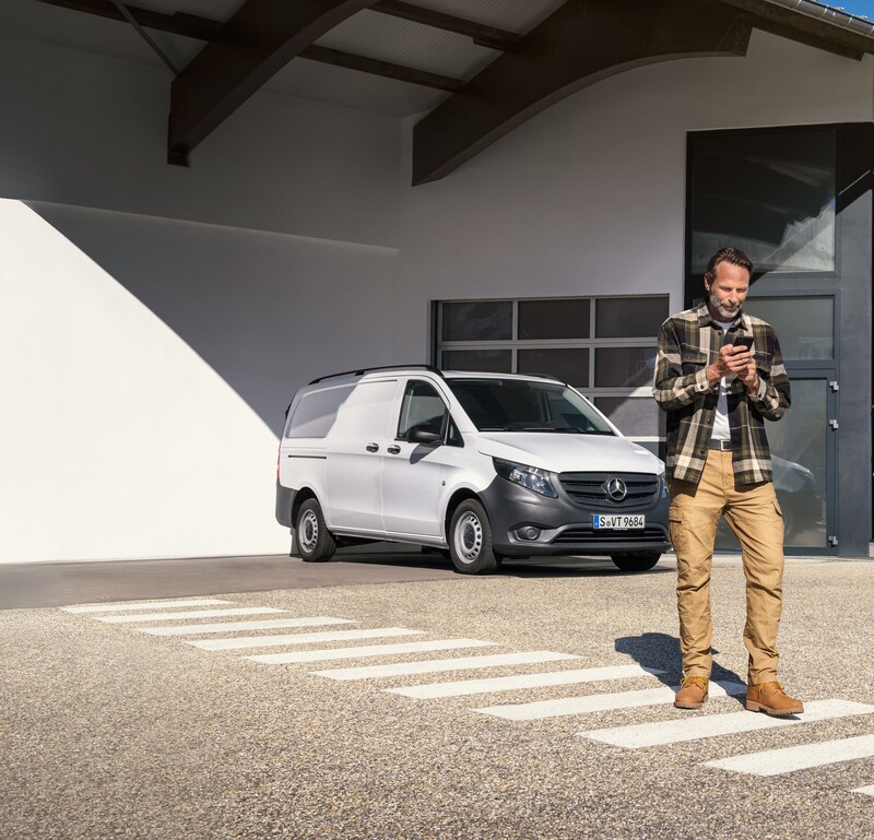 Mercedes-Benz | Wartung | Terminbuchung Ein Kunde bucht über sein Mobilgerät einen Termin, während er vor einem weißen Mercedes-Benz Vito steht.
