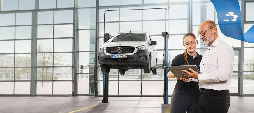 Mercedes-Benz | Wartung Zwei Mitarbeiter besprechen in der Werkstatt den Nutzfahrzeugservice an einem aufgebockten Mercedes-Benz Transporter.